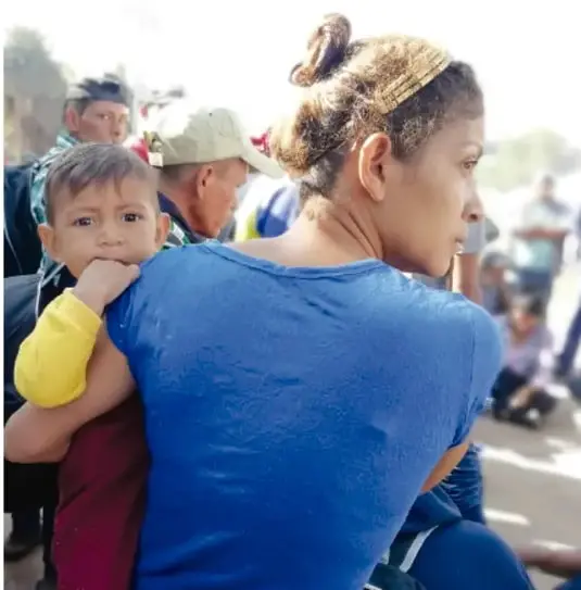Fotografía de una mujer cargando a un niño pequeño entre una multitud, representando una situación de migración o desplazamiento.