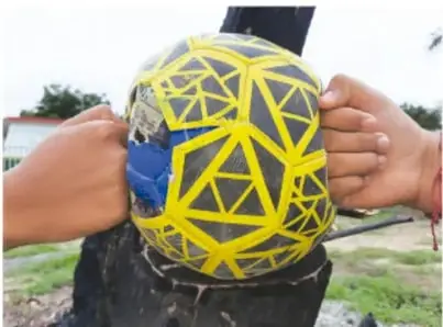 Manos apretando una esfera cubierta con banda elástica amarilla sobre un tronco, ilustrando deformación.