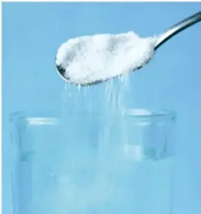 Cuchara con sal vertiéndose en un vaso con agua, ilustrando la solubilidad.