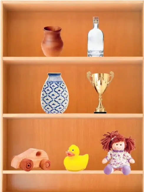 Repisa de madera de tres estantes. Arriba: vasija de greda color ladrillo y botella de vidrio transparente. Al medio: florero de cerámica con decoración azul y blanca, y trofeo dorado de metal. Abajo: auto de juguete de madera, patito de goma amarillo y muñeca de trapo con vestido floreado.