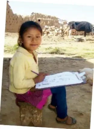 Fotografía de una niña sentada en un banco de barro escribiendo en un cuaderno, con un paisaje rural de adobes y ganado al fondo.