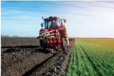 Fotografía de una máquina agrícola roja (tractor o cosechadora) trabajando en un campo extenso, representando la agricultura mecanizada o moderna.