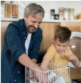 Fotografía de un adulto mayor y un niño lavando trastes en la cocina, con expresión amable.