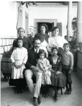Fotografía antigua en blanco y negro de una familia numerosa posando en el interior de una casa, con adultos y niños vestidos de época.