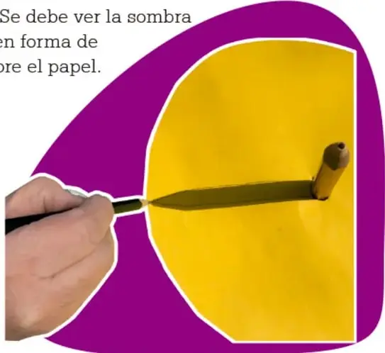 Fotografía de una mano marcando con un plumón la sombra de un cilindro sobre una hoja amarilla.