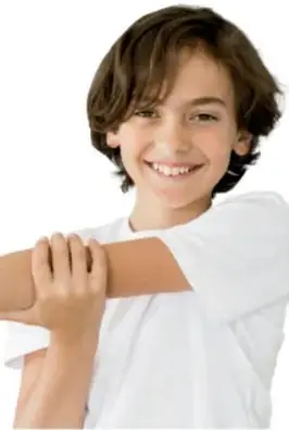 Niño sonriente con playera blanca realizando un estiramiento de brazo cruzado sobre el pecho.