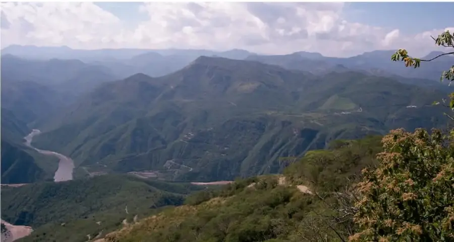 Fotografía de un paisaje montañoso con un río que serpentea en el fondo de un valle, rodeado de vegetación y montañas. Representa una cuenca hidrográfica en su estado natural.