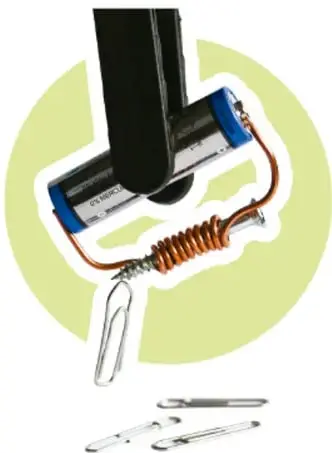 Fotografía de un electroimán casero: un tornillo con alambre de cobre enrollado conectado a una pila mediante cinta azul, atrayendo un clip metálico.