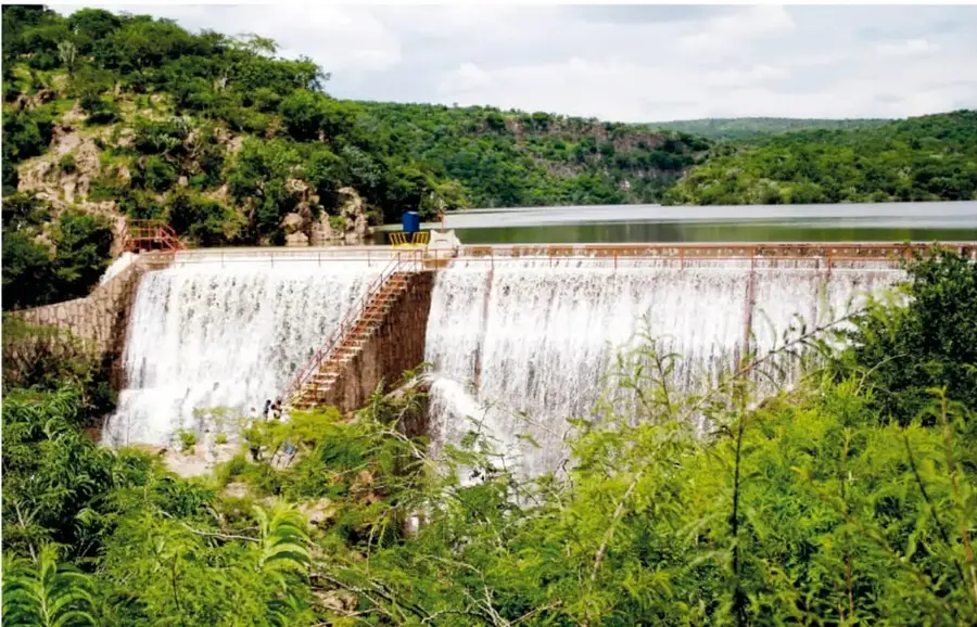 Fotografía de la presa Malpaso con agua desbordando sobre su muro, rodeada de vegetación verde y colinas de la sierra del Laurel.