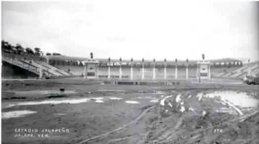 Fotografía antigua con leyenda «Estadio Xalapeño. Jalapa, Ver.»: gradas del estadio al fondo y terreno abierto con charcos al frente.