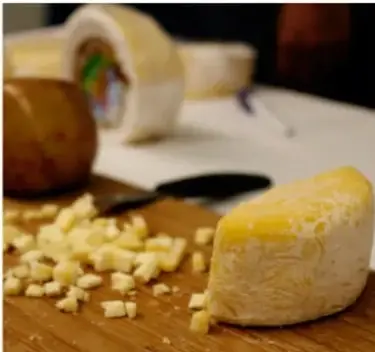 Fotografía de un bloque de queso amarillo cortado en cubos sobre una tabla de madera.