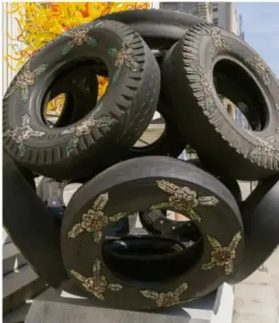 Fotografía de una escultura formada por neumáticos (llantas) apilados con figuras de mariposas doradas, representando una obra de arte reciclado.