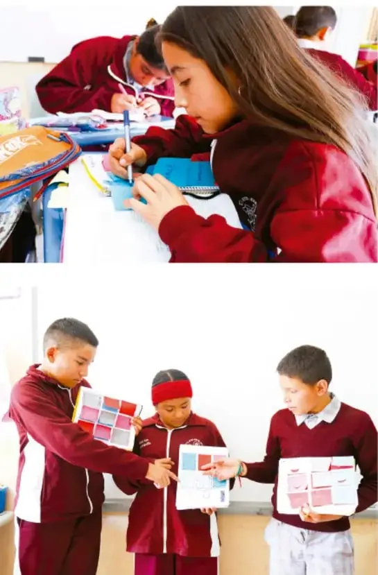 Estudiantes de telesecundaria con uniforme rojo trabajando en sus cuadernos en el aula.