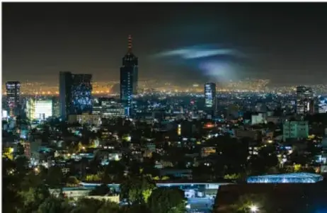Fotografía nocturna de una ciudad con luces y destellos luminosos en el cielo, asociada al fenómeno de las luces que se observan durante los temblores.