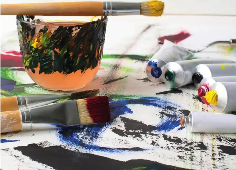 Fotografía de paleta de pintor con manchas multicolores, pinceles y tubos de pintura, evocando trabajo artístico.