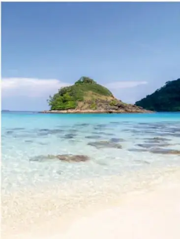 Fotografía de una playa virgen con agua turquesa y una isla rocosa.