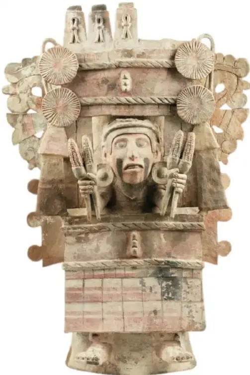 Escultura antigua de piedra o barro de una deidad del maíz: figura con tocado alto decorado con mazorcas, que sostiene una mazorca en cada mano, sobre una base tipo templo.
