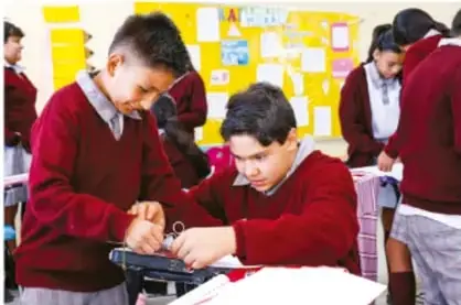 Fotografía de estudiantes de telesecundaria trabajando con material impreso y equipos, en actividad colaborativa de proyecto.