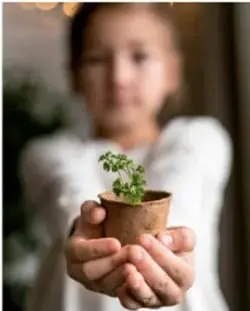 Niña sosteniendo una maceta con una planta pequeña.