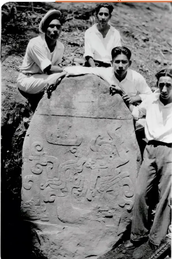 Fotografía en blanco y negro de cuatro hombres de pie junto a la Estela 3 de Izapa, cerca de Tapachula, Chiapas. La estela es una gran piedra tallada con relieves de figuras y símbolos olmecas.