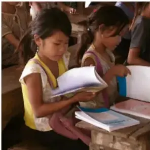 Fotografía de dos niñas sentadas en el suelo del salón, revisando cuadernos y libros durante una actividad escolar.