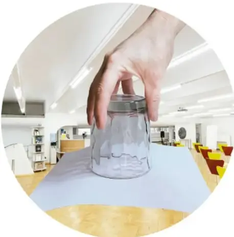 Mano sosteniendo un vaso de vidrio con agua cubierto por una hoja de papel, mostrando el experimento de presión atmosférica.
