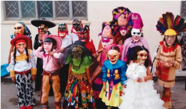 Grupo de niñas y niños disfrazados con máscaras, sombreros y trajes coloridos, como parte de una celebración o representación comunitaria.
