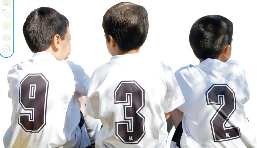 Tres niños de espaldas con camisetas deportivas blancas que llevan los números 9, 3 y 2.