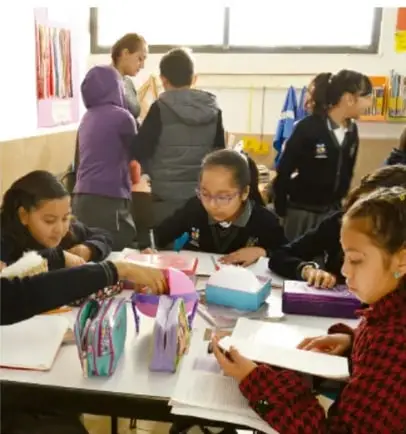 Estudiantes en el aula, sentados en grupo, escribiendo y colaborando en una actividad.