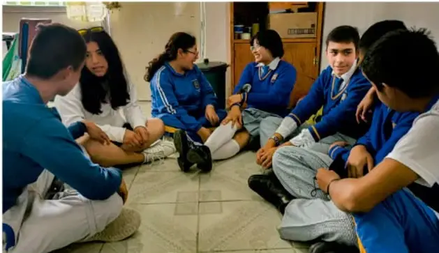 Fotografía de un grupo de estudiantes de telesecundaria sentados en círculo en el suelo, conversando; probablemente ensayo de la tertulia. Crédito: Luis Eduardo García Perell, IMJBCA.