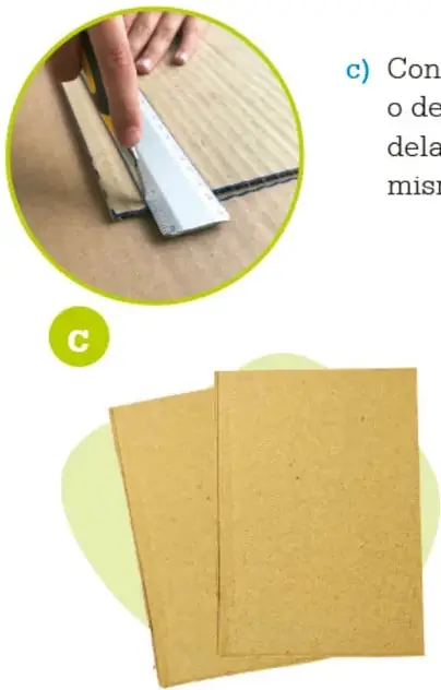 Manos cortando cartón rígido con un cúter sobre una superficie de madera.