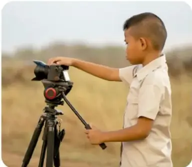 Fotografía de un niño sonriente escribiendo en una hoja.