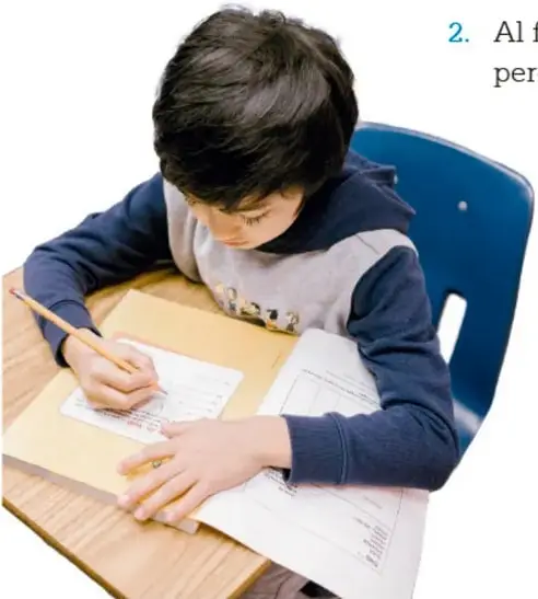 Niño sentado en un pupitre escribiendo en su cuaderno, con lápiz en mano.