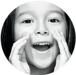 Fotografía en blanco y negro de una niña sonriente con las manos en el rostro.