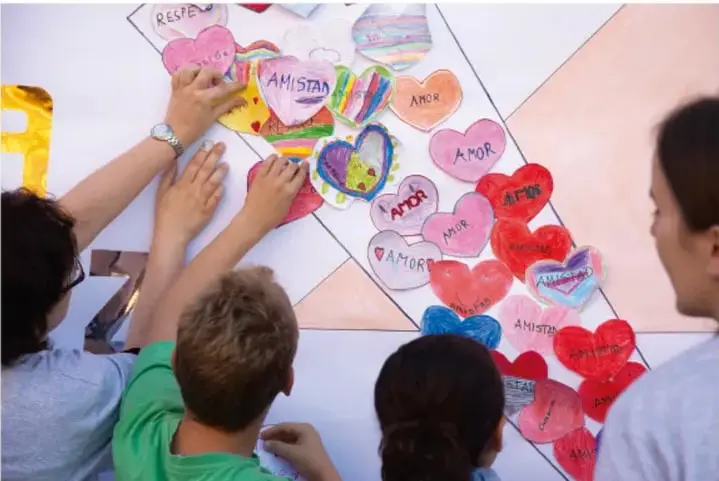 Fotografía de estudiantes colocando corazones de papel con palabras como amor, amistad y respeto en un mural escolar, representando valores de la cultura de paz.