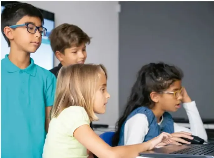 Tres estudiantes de primaria observan una computadora portátil en el aula.