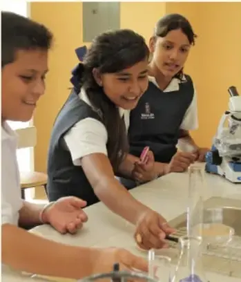 Fotografía de tres estudiantes trabajando en equipo con material de laboratorio sobre una mesa.
