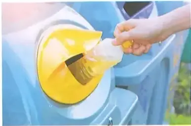 Persona depositando una botella plástica en un recipiente de reciclaje.