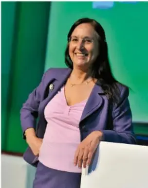 Retrato de una científica mexicana sonriente, con blusa rosa y saco morado, apoyada en una barandilla.
