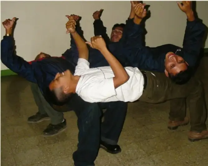 Fotografía de cuatro estudiantes de secundaria formando una figura humana: tres de ellos sostienen a un compañero acostado en el aire, con los brazos levantados, en un patio escolar.