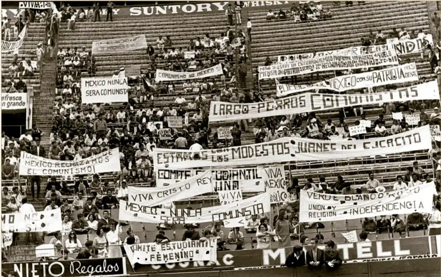 Fotografía en blanco y negro de gradas de un estadio llenas de personas con pancartas lemas como 'México nunca será comunista', 'Viva Cristo Rey', 'Fuera comunistas' y 'Estamos los modestos jóvenes del Ejército', correspondiente a una manifestación anticomunista del 8 de septiembre de 1968.