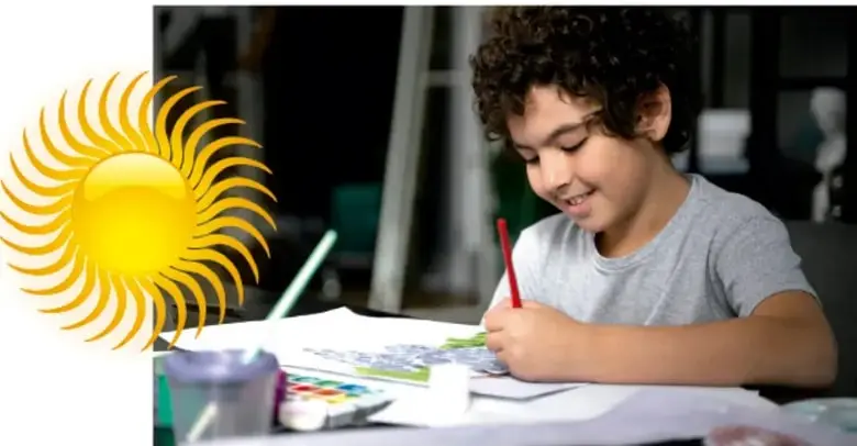 Niño sonriente dibujando o coloreando un plano sobre una mesa con lápices de colores.