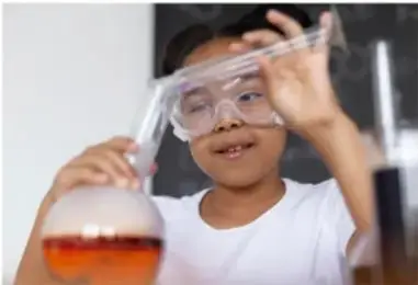Fotografía de una estudiante con gafas de seguridad realizando una práctica de laboratorio con matraz y tubo de ensayo.
