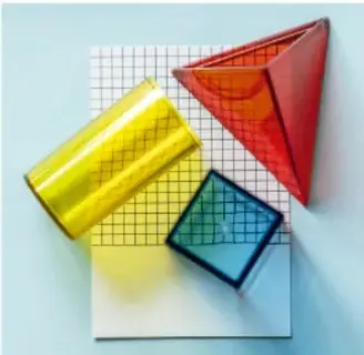 Figuras geométricas transparentes (prisma cuadrado amarillo, pirámide roja, lámina azul) sobre una cuadrícula, ejemplo de figuras tridimensionales.