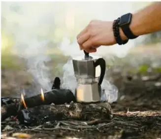 Fotografía de una persona calentando una cafetera sobre una fogata, ejemplo de transmisión de calor.
