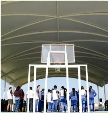 Fotografía de una cancha de básquetbol techada con un grupo de jóvenes estudiantes de secundaria uniformados (pantalón azul) observando o participando en una actividad deportiva, ilustrando el contexto de comunidades deportivas mencionado en el ejercicio 7.