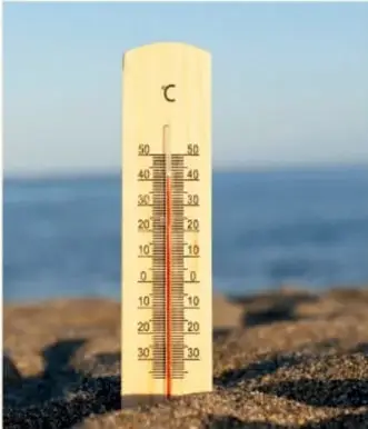 Termómetro sobre arena junto al mar, ilustrando la medición de temperatura.