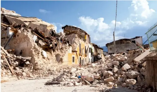 Fotografía de edificios destruidos y escombros tras un desastre, con cielo nubes al fondo.