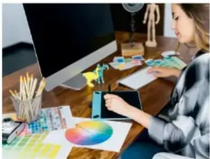 Mujer trabajando en el diseño de un proyecto frente a un monitor, con muestras de color y materiales de diseño.