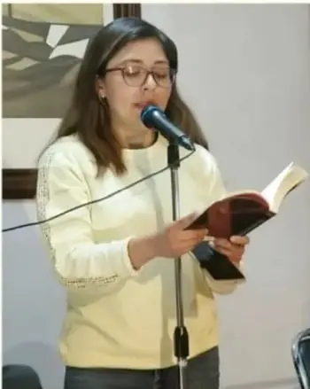 Fotografía de una joven de lentes leyendo un libro frente a un micrófono